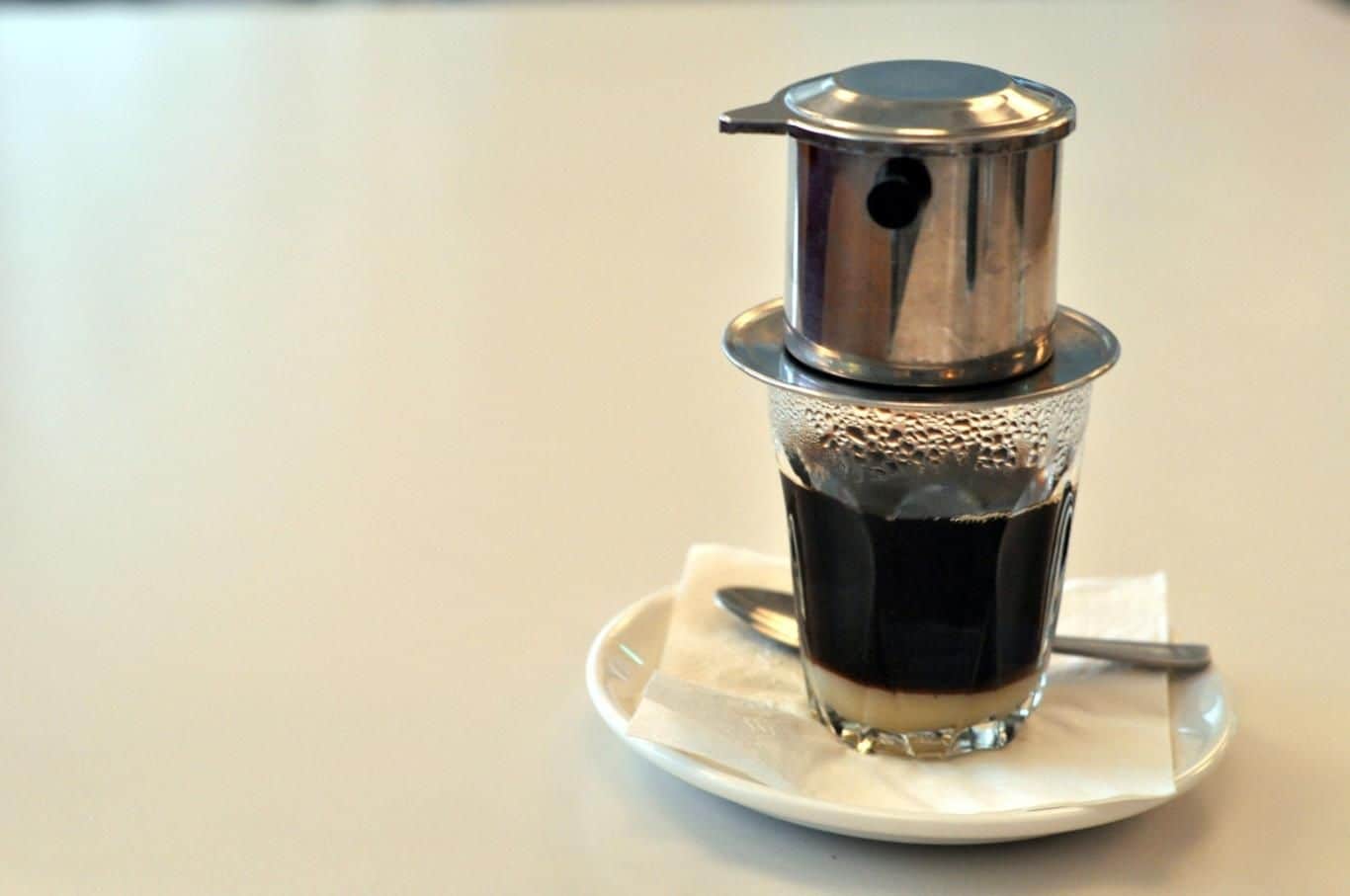 Close-up view of coffee drops falling from a traditional phin filter into a cup.